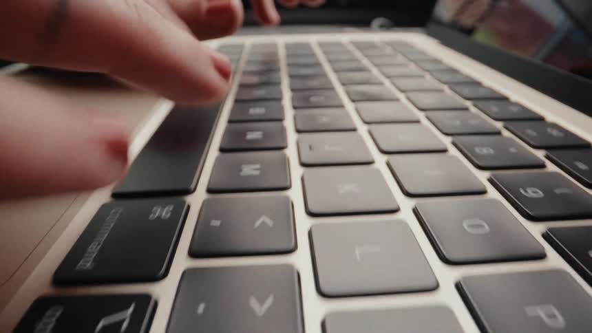 Extreme close-up shot of a woman's fingers with red nails typing on a laptop keyboard as the camera slowly pans back