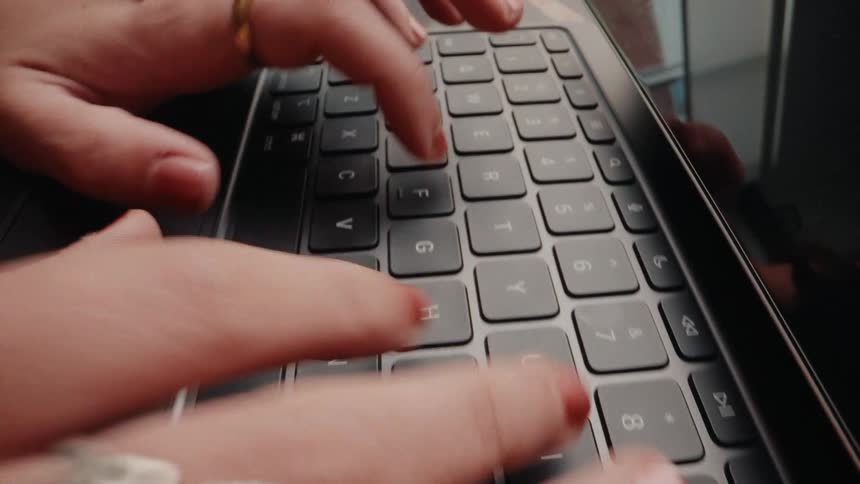 A dynamic close-up shot of a person's hands with red nail polish and rings typing quickly on a computer keyboard
