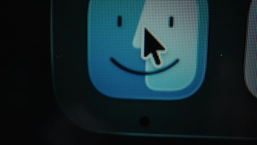 An extreme macro close-up of a computer screen shows a mouse cursor moving over the Apple macOS Finder icon