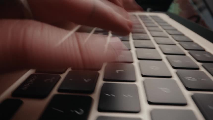 An extreme close-up time-lapse of a person's fingers typing quickly on a laptop keyboard and using the trackpad