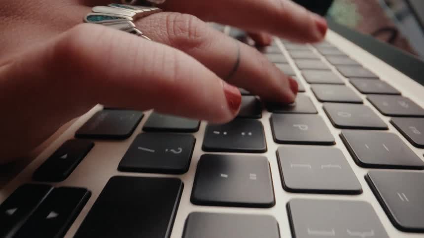 A slow-motion close-up shot of hands with red nail polish typing on a laptop keyboard