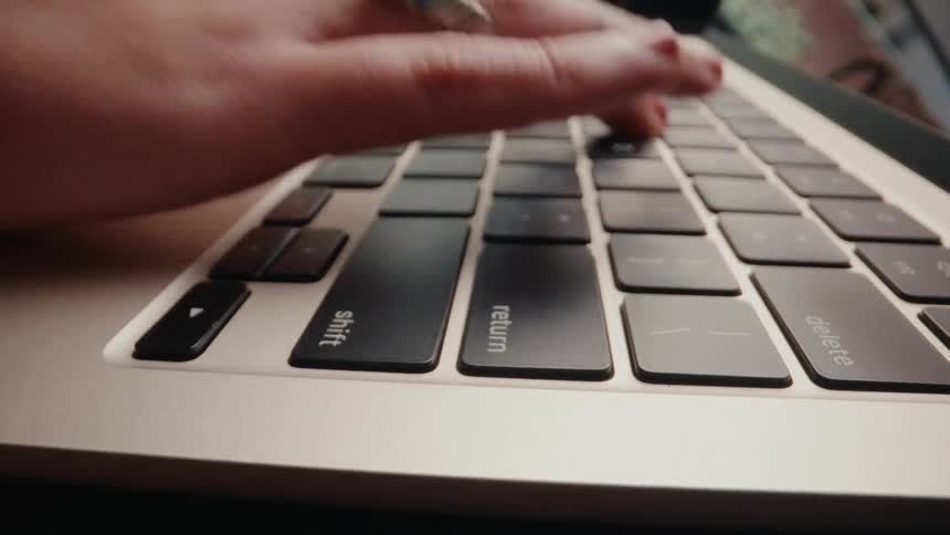 A dynamic extreme close-up shot of a person's hands typing quickly on a laptop keyboard before using the trackpad