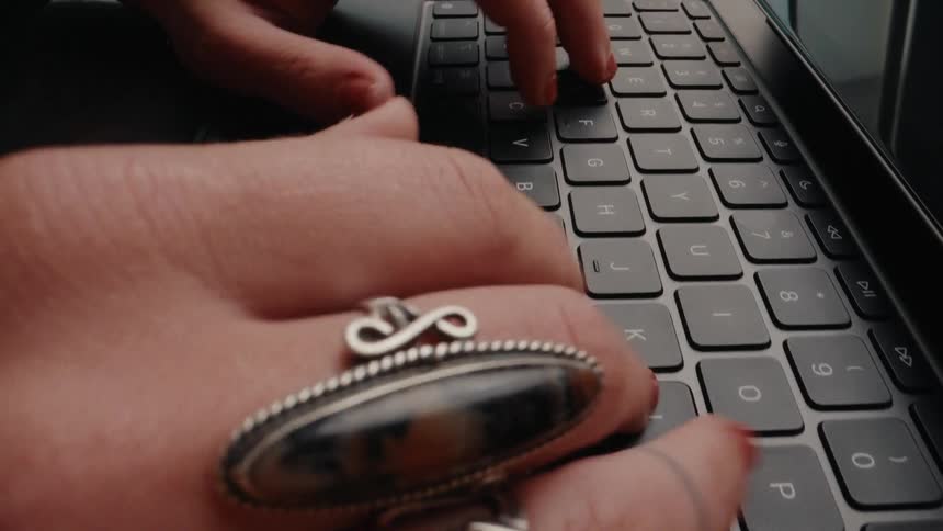 Close up of a woman's hands with stylish rings and red nail polish opening a tablet and typing on the keyboard