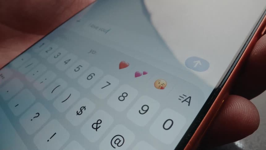 Extreme close-up of a finger typing and sending an 'I love you!' text message on a smartphone screen