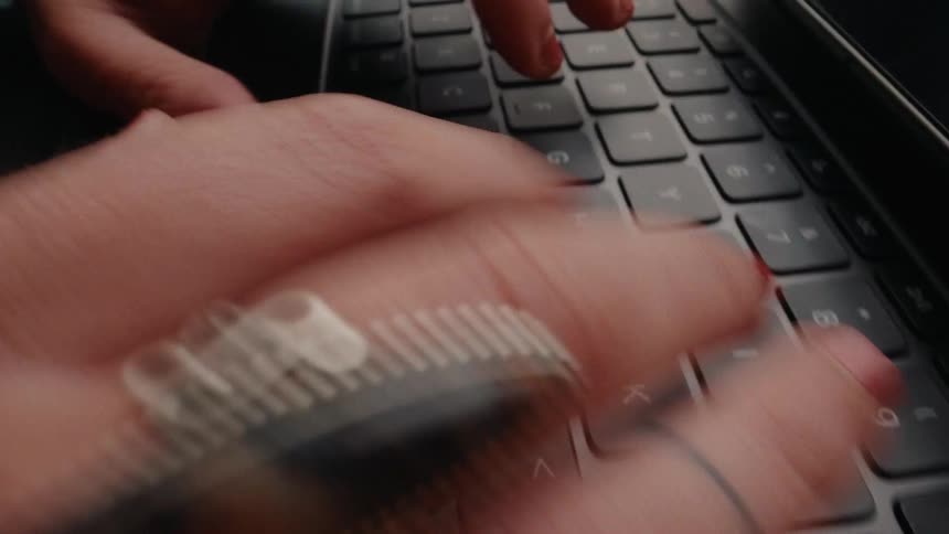 A close-up shot of a person with red nails and stylish rings typing rapidly on a laptop keyboard