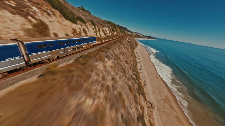 An exhilarating FPV drone shot chases a passenger train as it speeds along the picturesque California coastline next to the ocean
