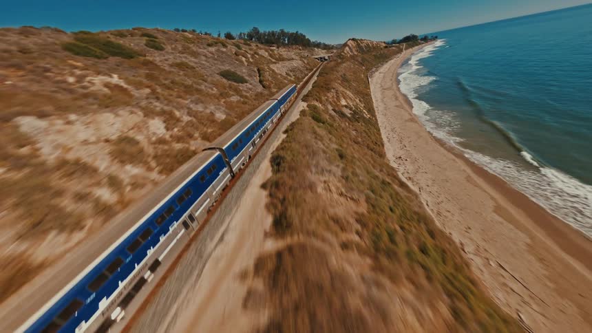 A high-speed FPV drone flies alongside the Pacific Surfliner train as it travels along the stunning California coast
