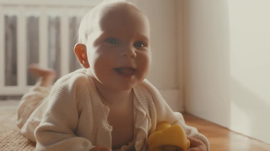 An adorable baby lying on the floor in a sunlit nursery smiles and laughs with pure joy