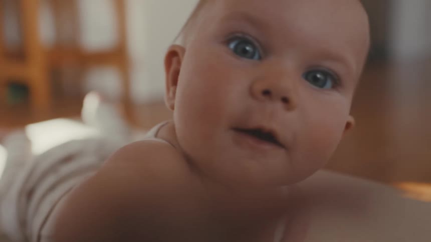 An adorable baby with big blue eyes smiles and curiously reaches for the camera in slow motion