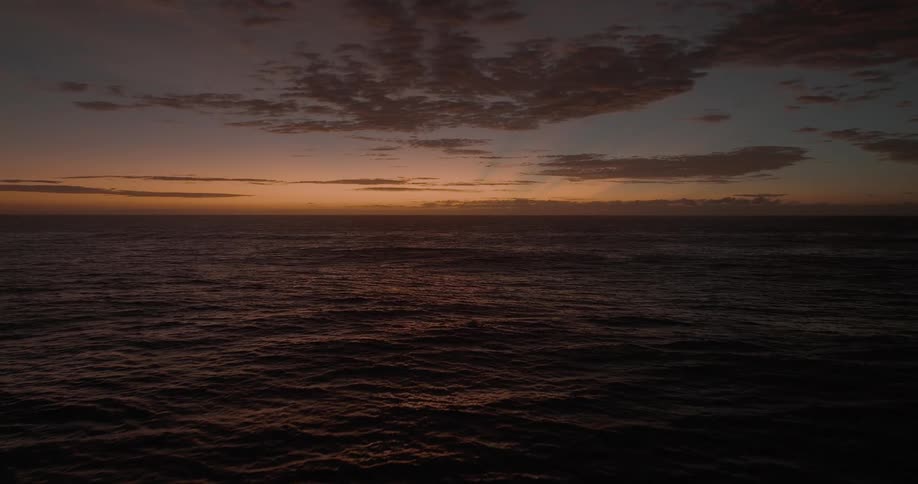 A tranquil ocean scene at dusk with gentle waves reflecting the warm glow of the sunset