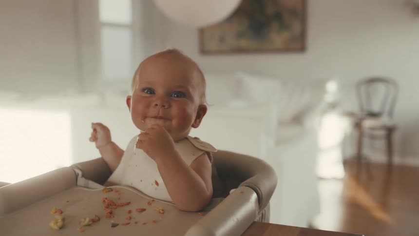 Close-up of a smiling baby enjoying a messy meal in a high chair