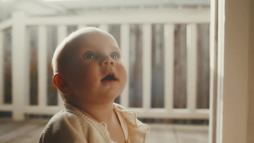 A close-up shot of a curious baby sitting on a woven rug and playing with a yellow rubber duck, looking up in wonder as soft sunlight streams in