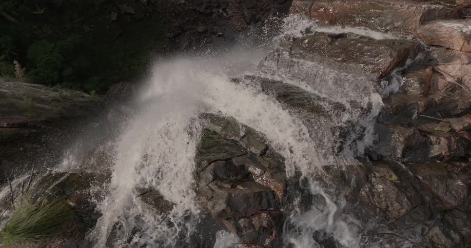 A powerful waterfall crashes over rugged rocks in a dramatic slow-motion aerial view