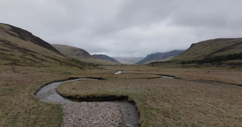 A slow aerial push-in shot follows a meandering river as it winds its way through a vast, remote valley under an overcast sky