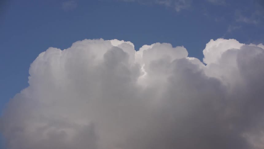 A large white cumulus cloud slowly builds and expands against a clear blue sky