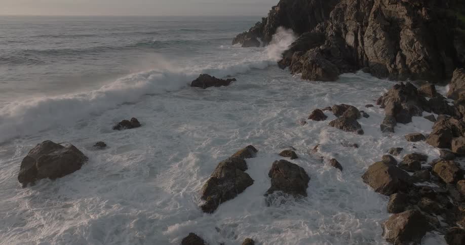 A powerful turquoise ocean wave crashes against a rocky shoreline in stunning slow motion