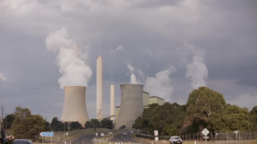 Smoke and steam billow from the cooling towers of a large power plant under a cloudy, grey sky