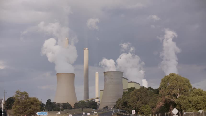 A large coal-fired power station with massive cooling towers and smokestacks releasing thick plumes of steam into the overcast sky