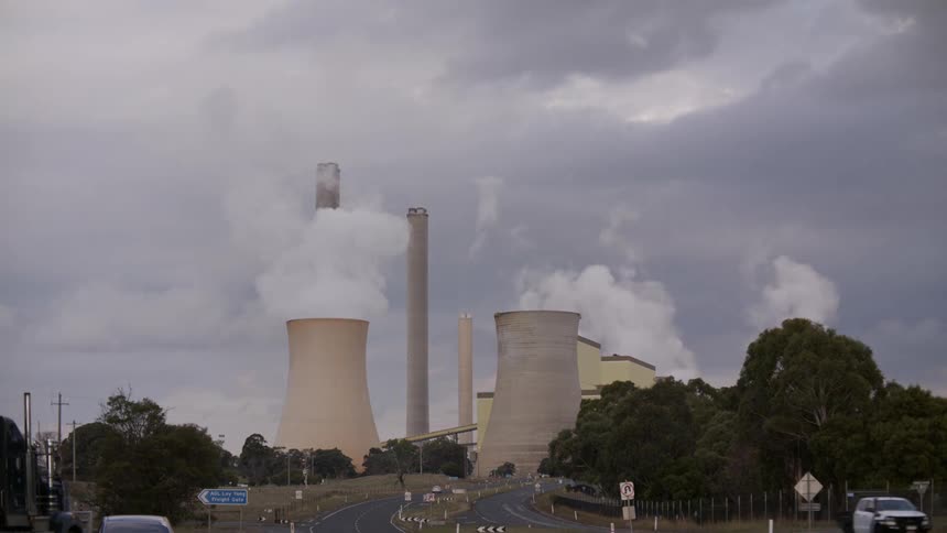A time-lapse view shows thick smoke billowing from the cooling towers and smokestacks of a power plant against a dark, cloudy sky