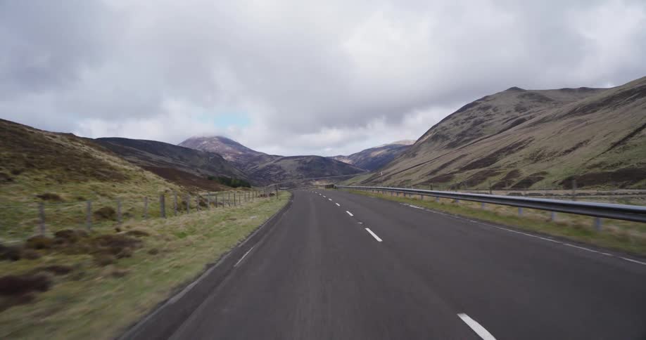 A serene POV drive along an empty road winding through the vast and dramatic landscape of the Scottish Highlands on a cloudy day