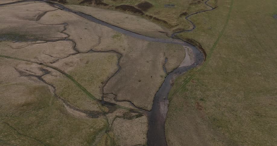 A slow-moving top-down aerial shot reveals a winding river and its tributaries flowing through a vast, grassy valley
