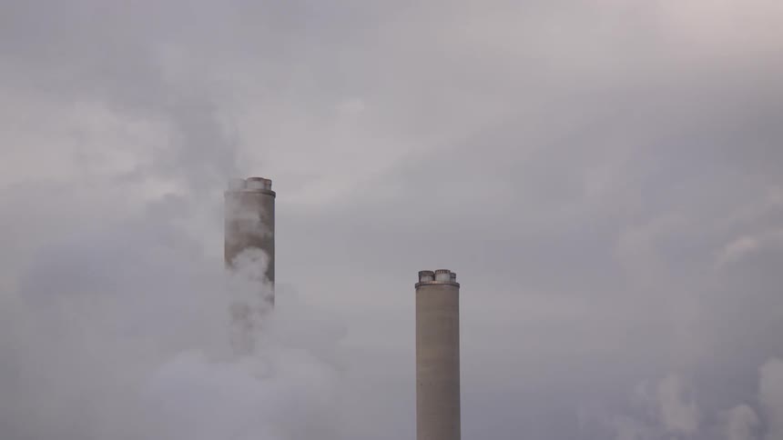 Two industrial smokestacks are almost completely obscured by the thick, white smoke they emit on a grey, overcast day