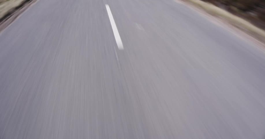 A close-up point-of-view shot of a vehicle speeding down an asphalt road, with the white lane lines blurring past in a seamless loop