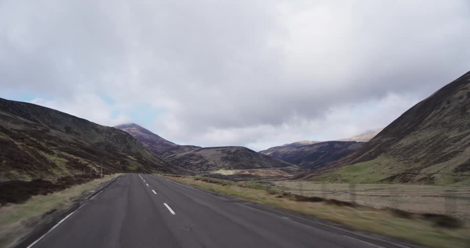 A point-of-view shot driving along a remote country road through a vast mountain valley on an overcast day