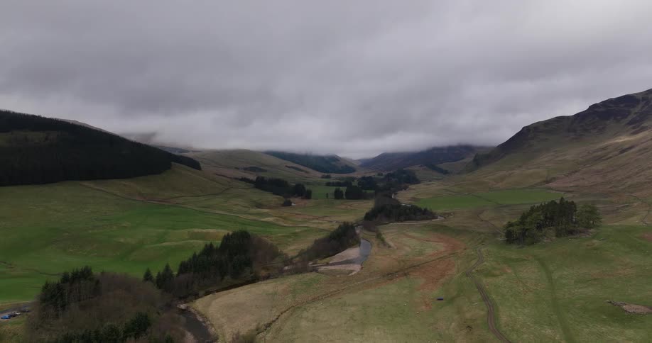 A serene aerial view of a winding river flowing through a vast, green mountain valley under an overcast sky