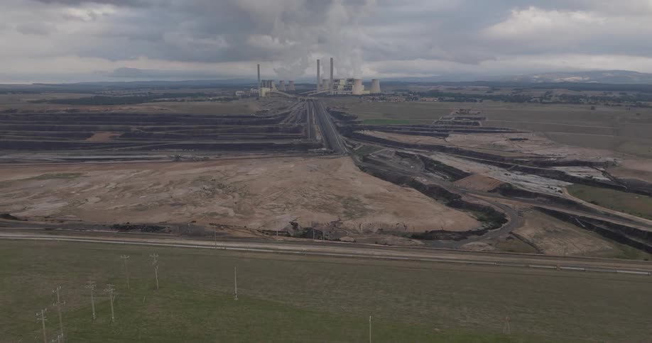 Wide aerial shot slowly tracking towards a large coal-fired power plant and its adjacent open-pit mine under an overcast sky