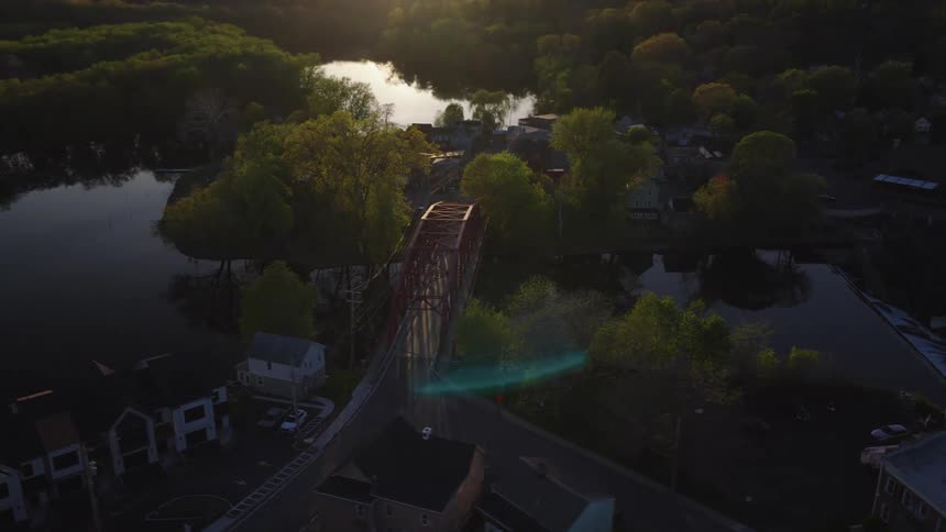Cinematic aerial pan over a picturesque red bridge and tranquil riverside town at sunrise