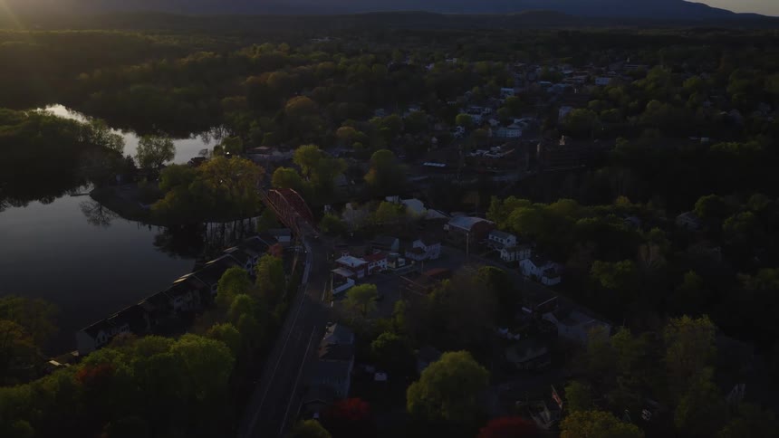 Aerial view of a picturesque small town nestled by a river with a red bridge during a golden sunset