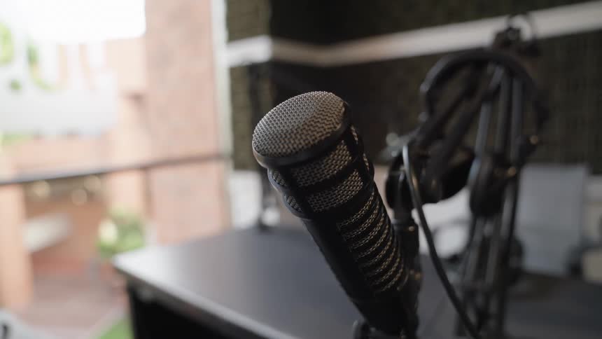 A professional broadcast microphone is shown in a close-up, static shot within a recording studio