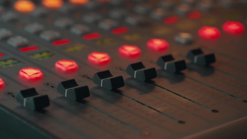 Shallow focus close-up of faders and glowing red lights on an audio mixing console in a studio