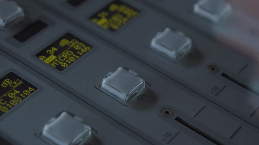 A close-up of a woman's finger turning off a red illuminated 'ON' button on a professional audio mixing console