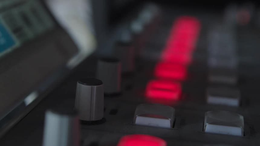 A close-up shot of a finger with sparkling nail polish turning off the glowing red lights on a soundboard