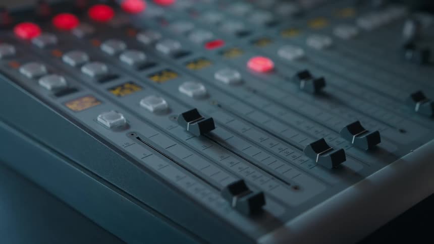 Close-up of a female hand adjusting the sliders on a professional audio mixing console in a studio