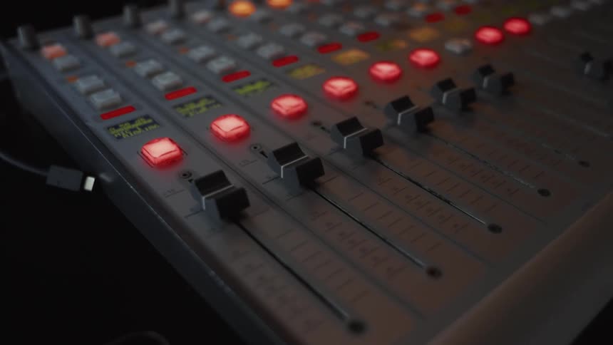 Slow dolly push-in on a professional audio mixing console with glowing red buttons in a dark studio