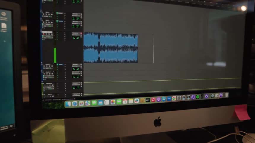 A slow push-in on a computer monitor displaying audio waveforms in a digital audio workstation inside a music recording studio