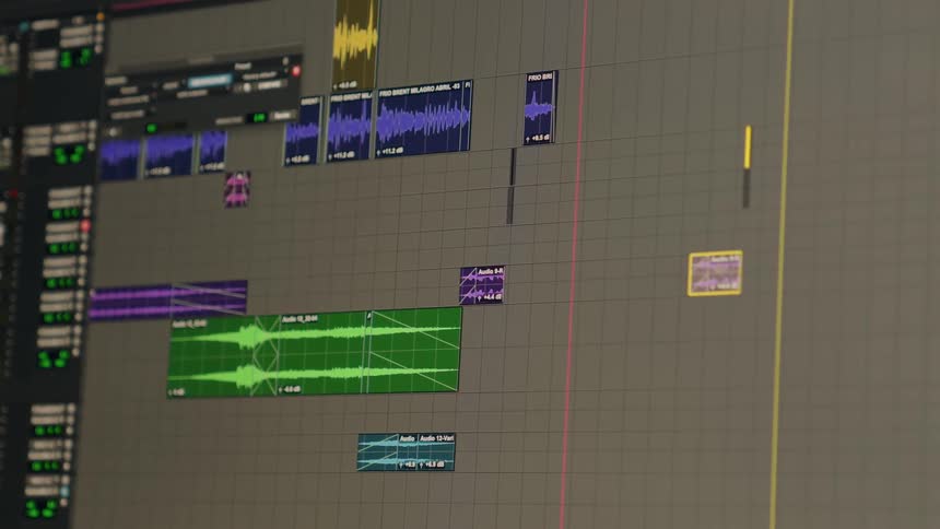 A close-up of a digital audio workstation timeline where a sound editor is moving and arranging colorful waveform clips