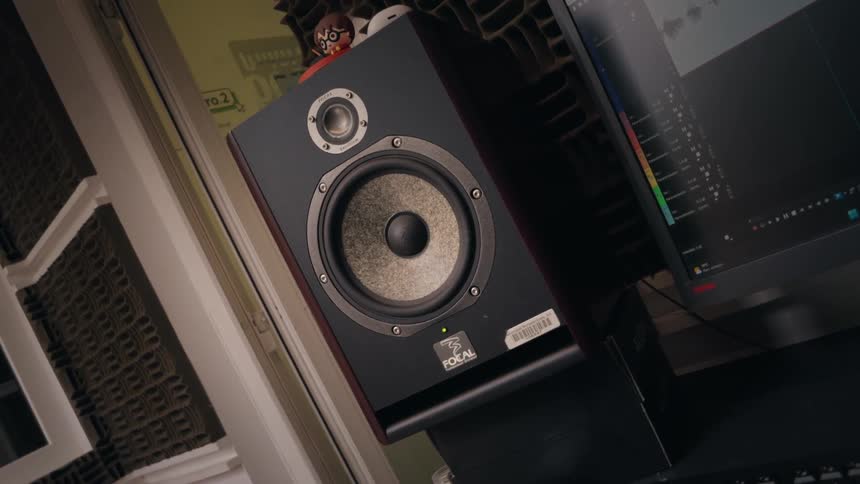 A dutch angle shot of a professional audio speaker vibrating while playing sound in a recording studio