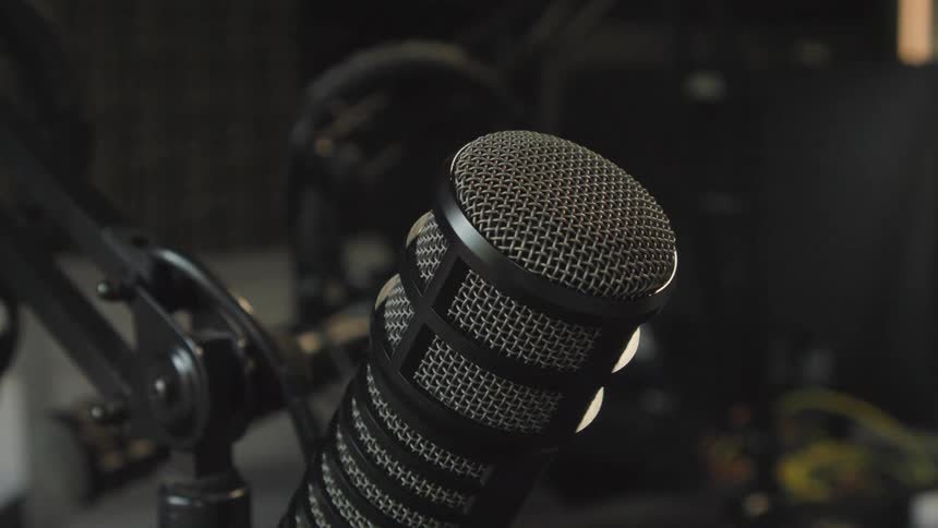 A close-up of a finger gently tapping a professional podcasting microphone in a recording studio