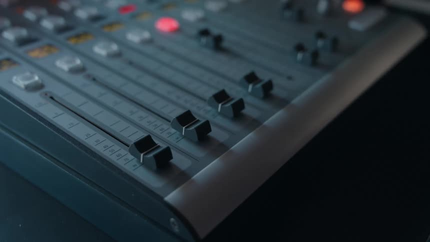 Close-up of a hand adjusting a fader on a professional audio mixing console in a studio