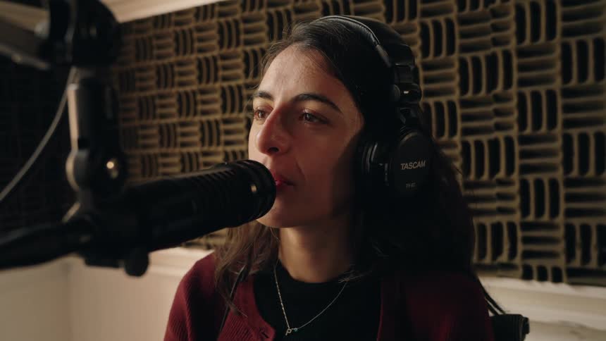 An intimate close-up of a woman with headphones speaking into a microphone inside a soundproof recording studio