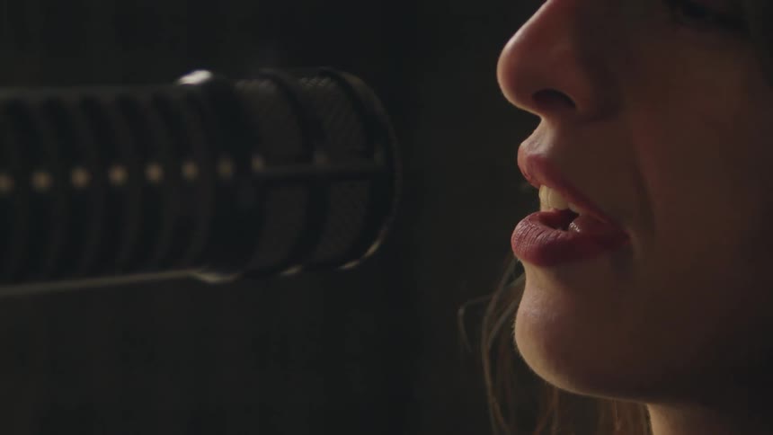 A close-up shot focuses on a woman's lips as she sings into a professional studio microphone