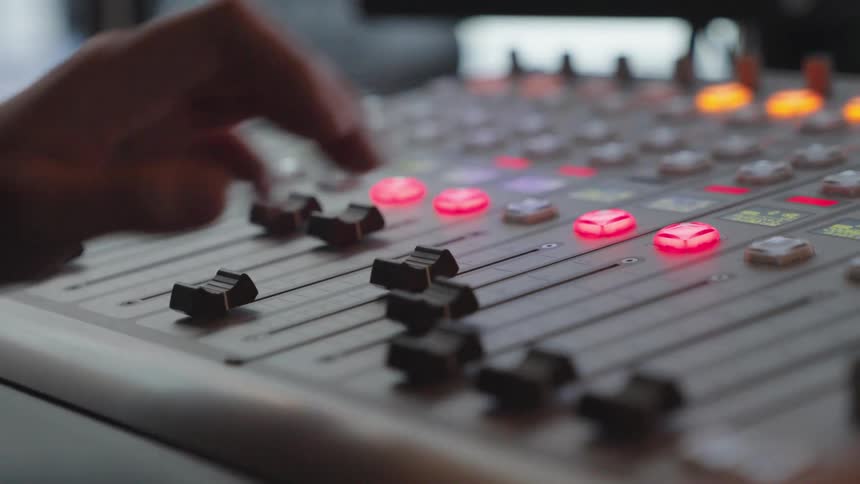 A sound engineer adjusts the faders and buttons on a professional audio mixing console in a studio