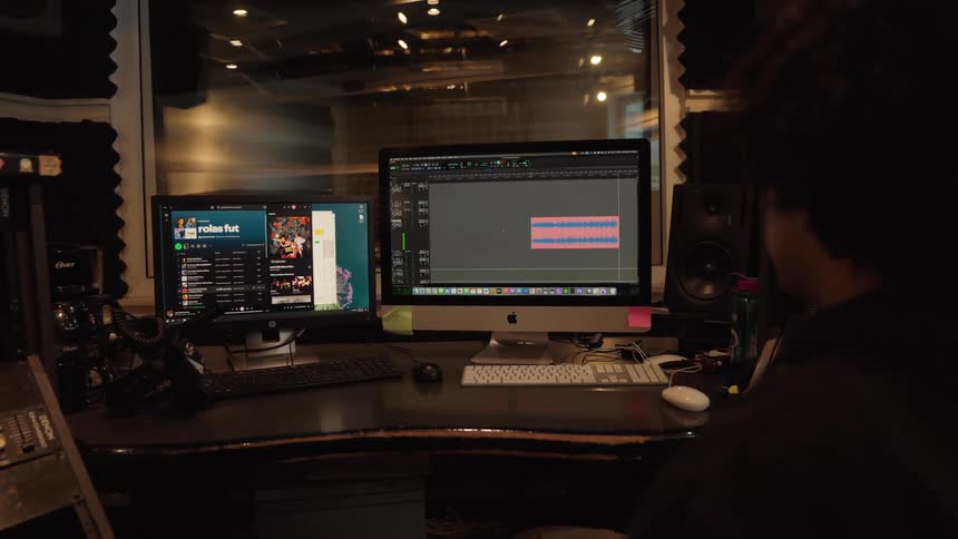 Over the shoulder view of a music producer editing an audio waveform on a computer in a professional recording studio
