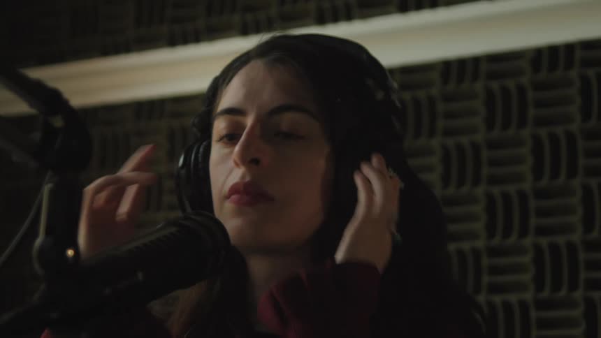 A young woman with long dark hair puts on headphones as she prepares to record in a soundproof studio