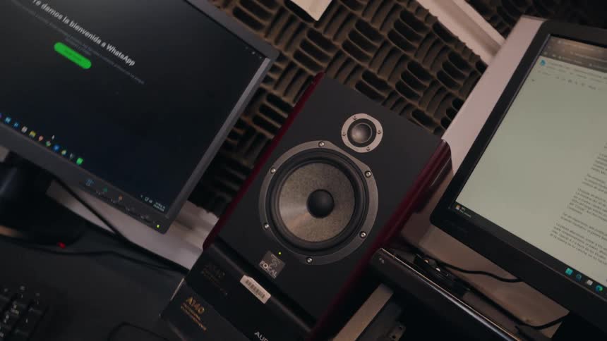 A slow zoom on a professional studio monitor speaker vibrating on a desk in a music production studio