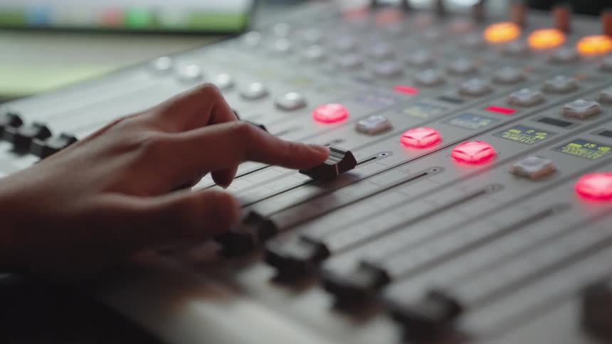 Close-up of a sound engineer's hand adjusting a fader on a professional audio mixing console